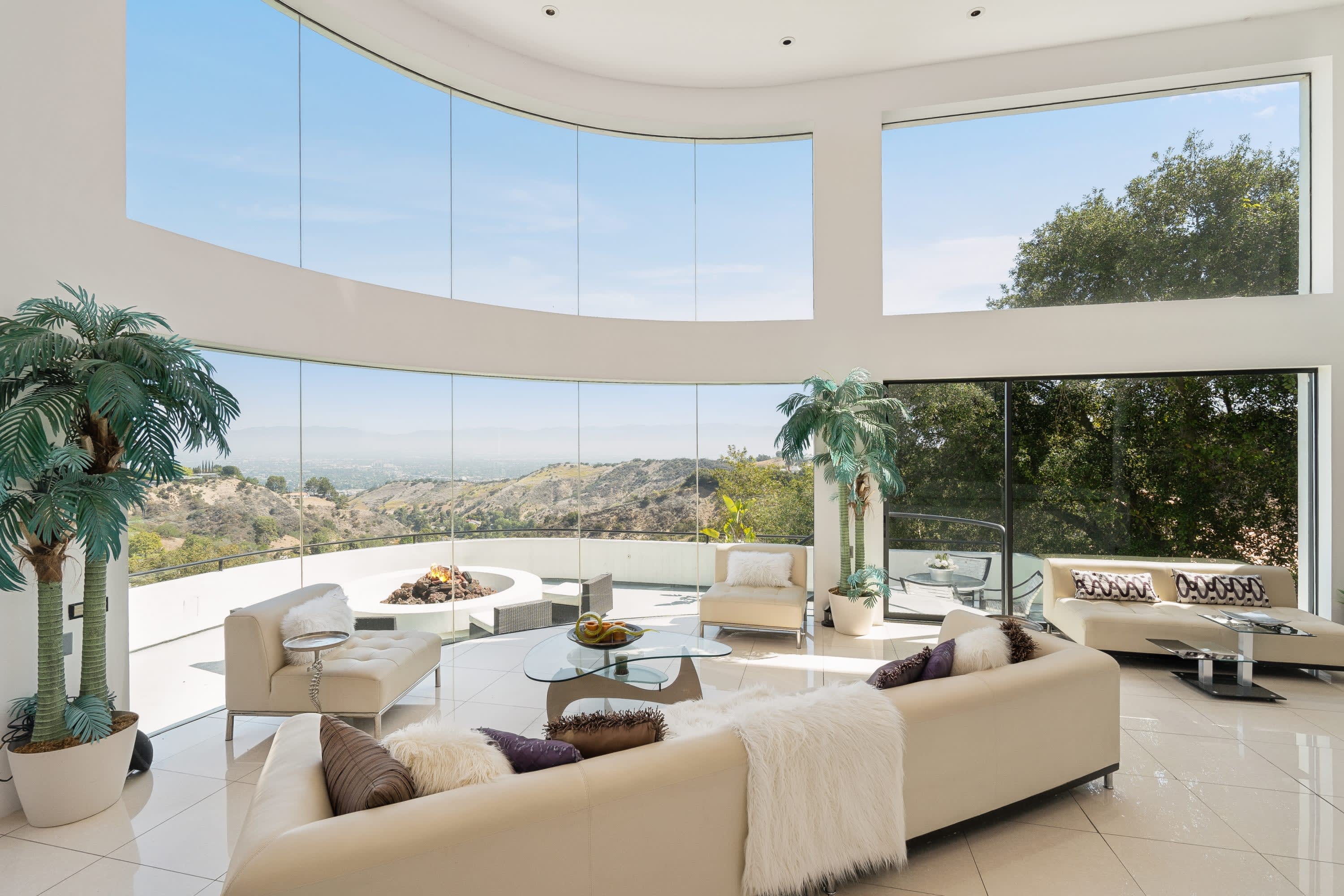 A living room with a fireplace, white couch, brown chairs, and a view of a garden