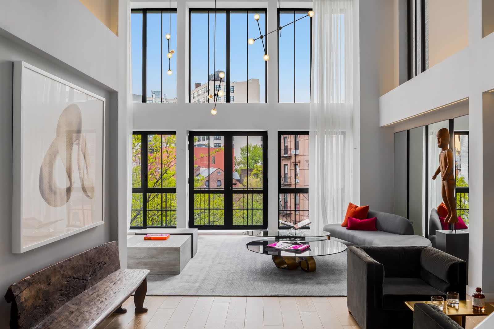 Luxury penthouse living room showcasing a two-story window wall, structural concrete low tables, a glass coffee table, minimalist light fixtures, and a mezzanine overlook.