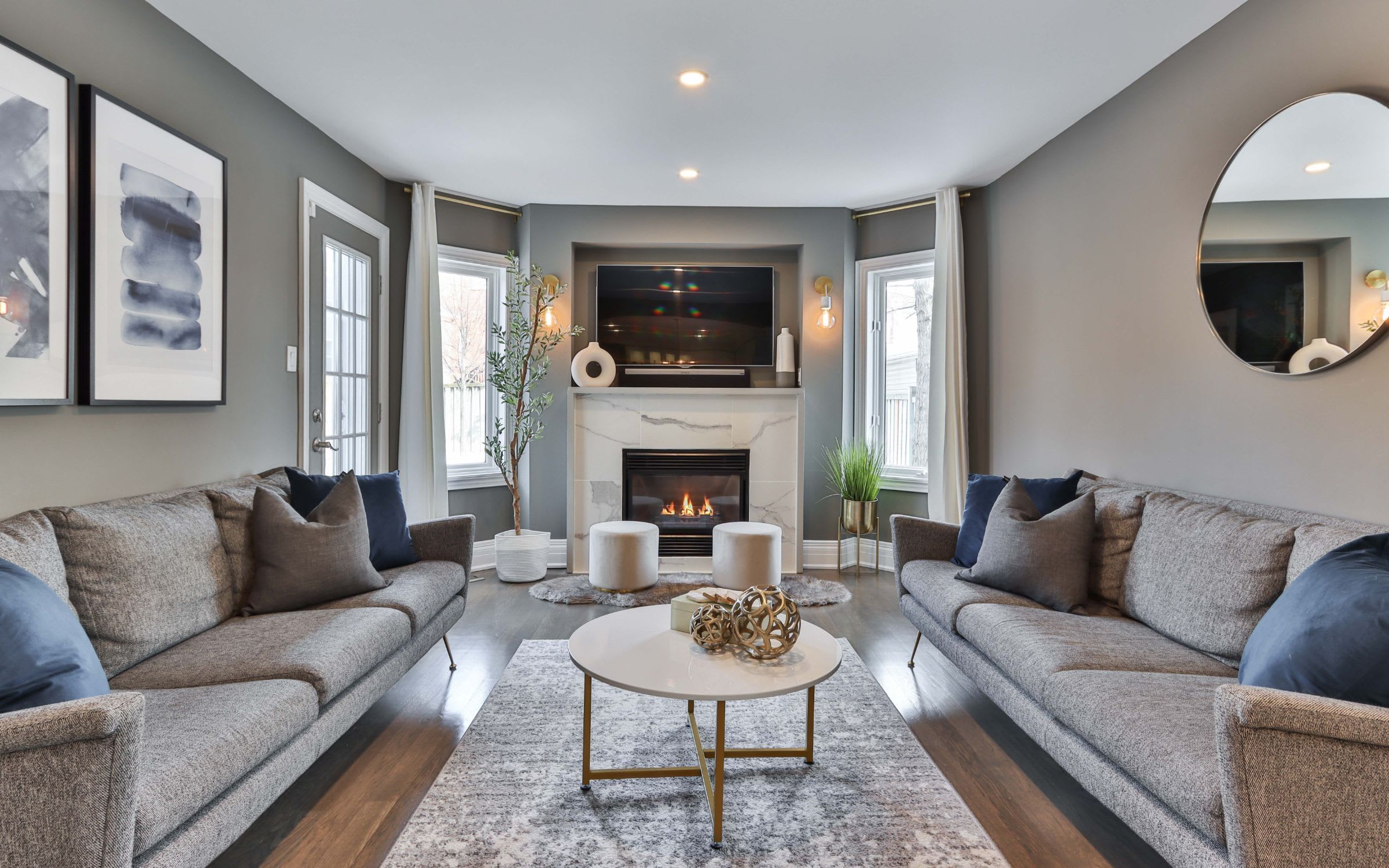 A cozy living room with two sofas around a coffee table. There is a fireplace, and a television is mounted above it.