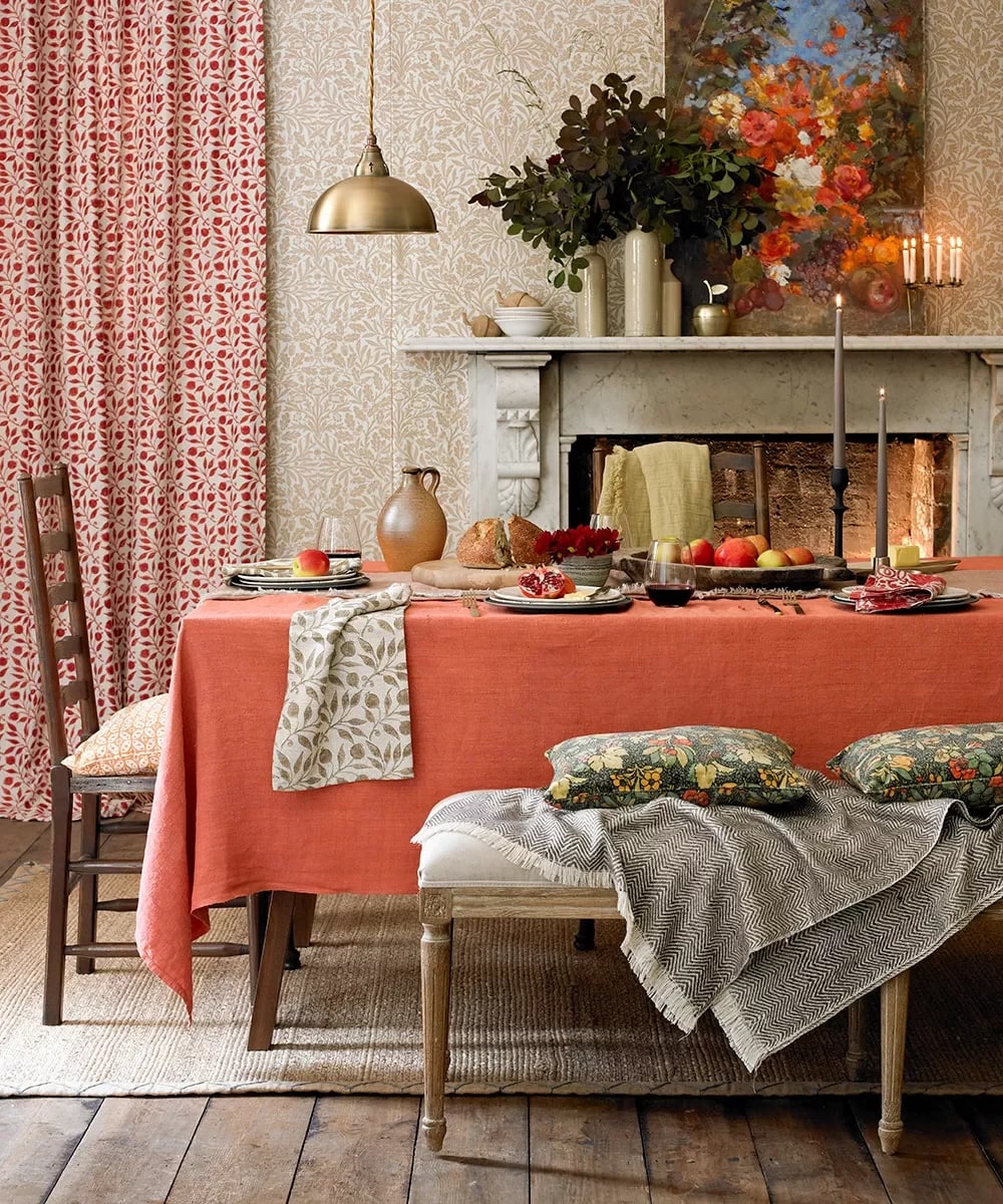 Dining room with a coral-covered table, botanical wallpaper, patterned curtains, and stone fireplace.
