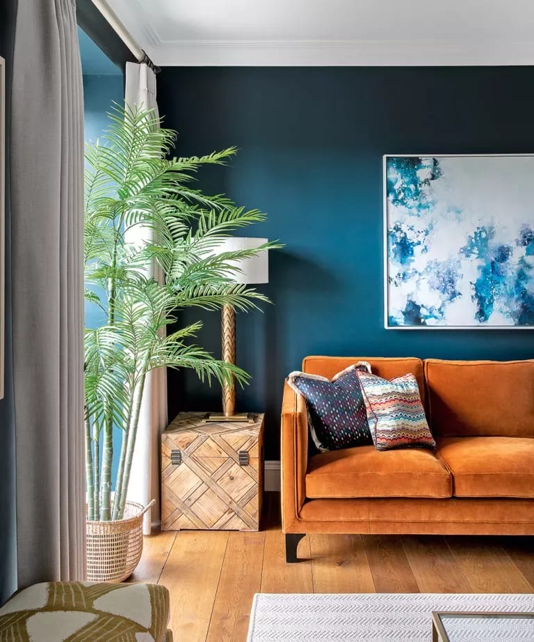 Living room with a burnt-orange sofa against a deep teal wall and a tall palm by the window.