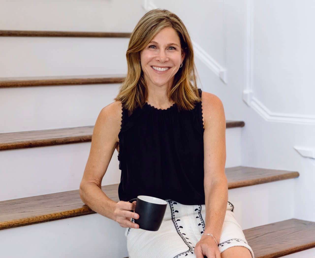 Marla Sewall seated on a staircase, holding a black mug.