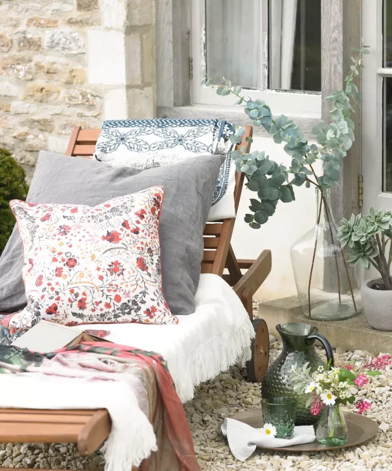Outdoor seating with patterned cushions, eucalyptus, flowers, and a rustic stone wall.