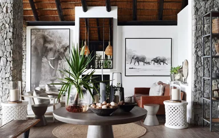 Living room with a thatched ceiling, stone walls, elephant artwork, and a round table with a tall plant.