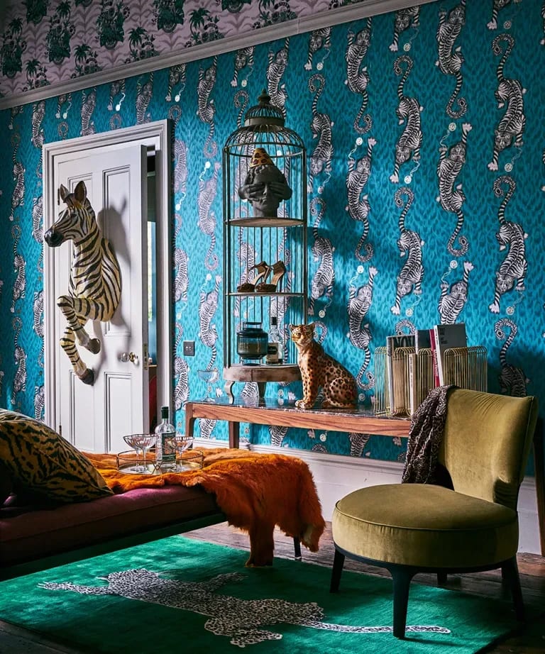 Eclectic living room with teal zebra wallpaper, animal sculptures, velvet seating, and a green patterned rug.