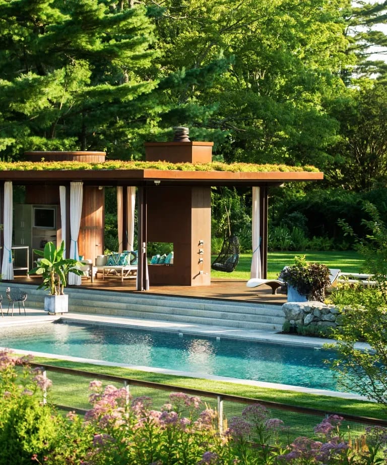 Modern home with an open patio and swimming pool amid lush trees and gardens.