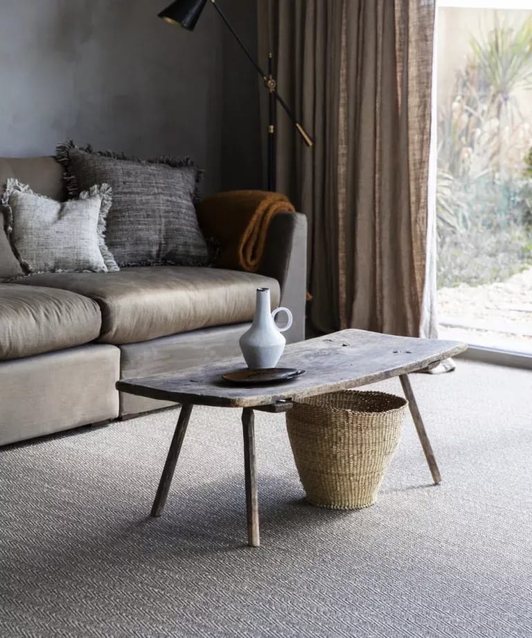 Living room with a gray sofa, rustic coffee table, white vase, woven basket, and tall window curtains.