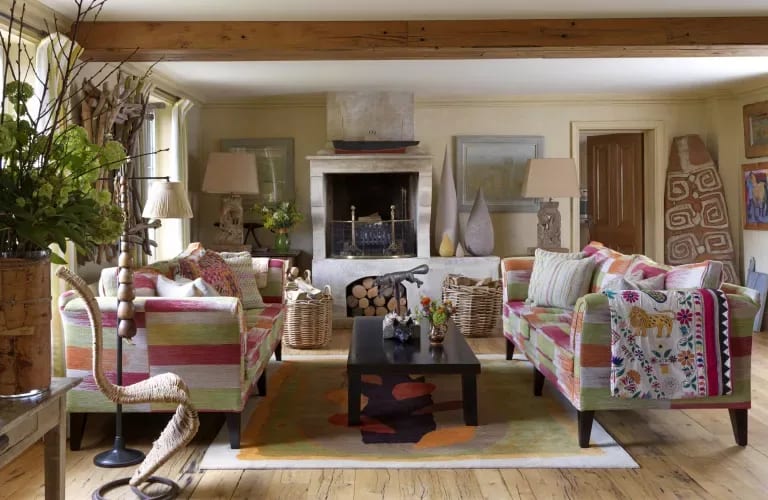 Living room with colorful patterned sofas, a stone fireplace, and an exposed wooden ceiling beam.
