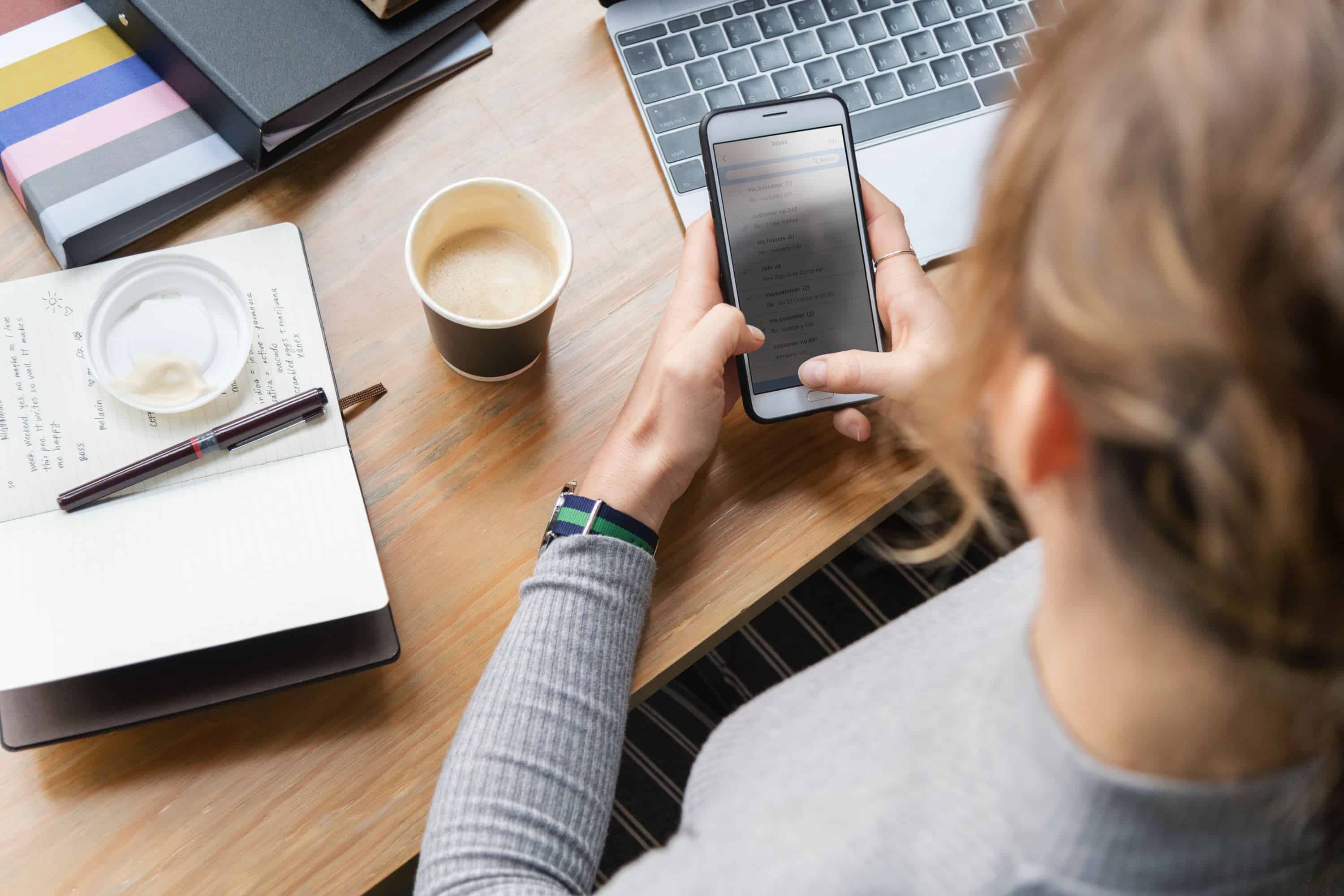 woman using her iphone with a notebook and a coffee cup in the background
