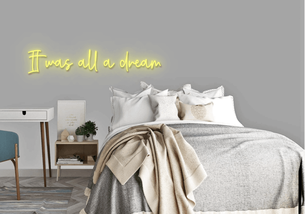 Staged bedroom with layered neutral bedding and a glowing yellow “It was all a dream” sign.