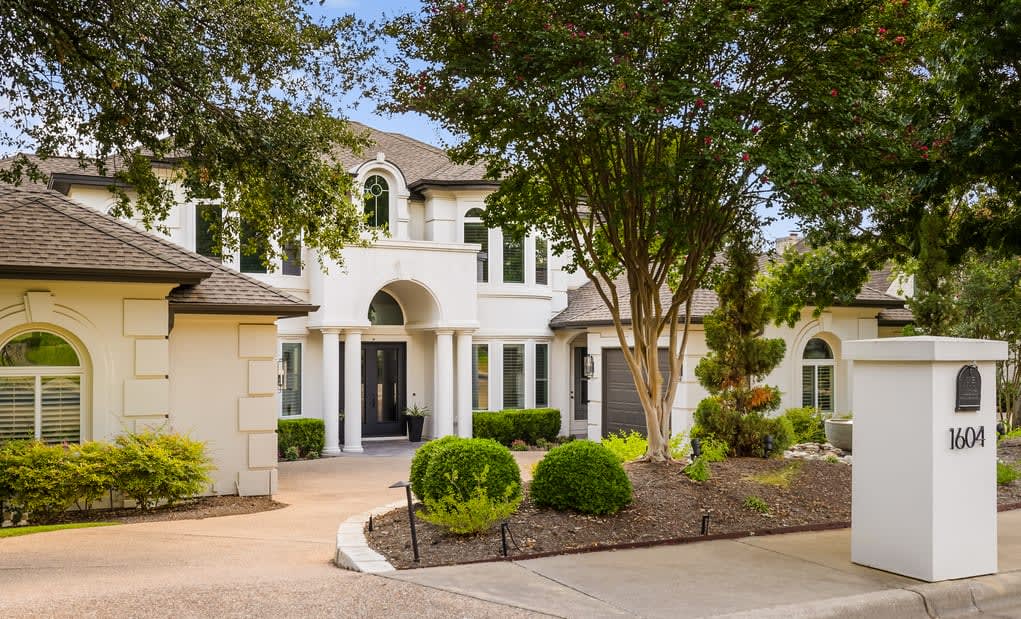 A serene white house with a driveway and lush green trees.