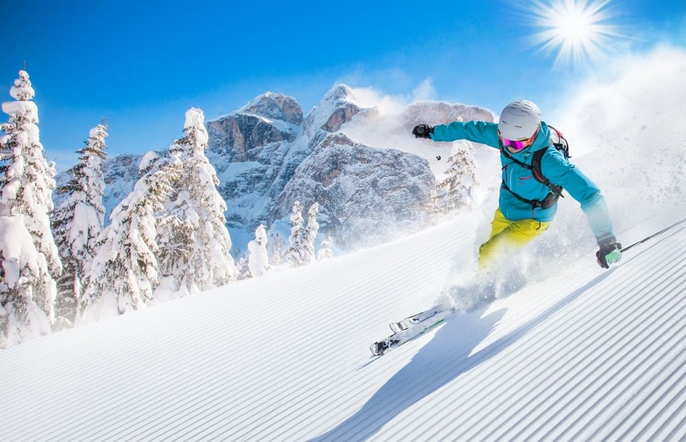 A person wearing a sky blue jacket and white helmet, skis down a snow-covered slope on a bright and sunny day.