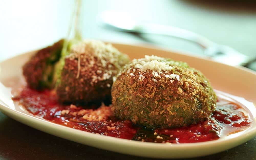 Plate of crispy arancini balls served on a bed of tomato sauce, topped with grated cheese.