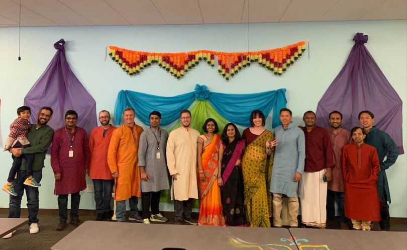 A group poses in traditional South Asian clothing beneath colorful fabric decorations.