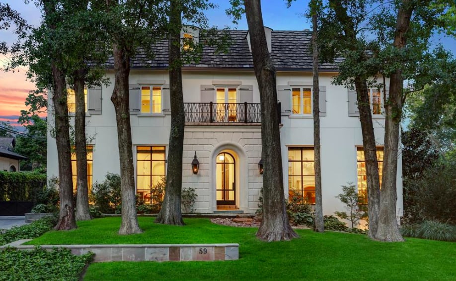 A three-story French-style mansion, with a white exterior, slate roof, balcony, and front lawn, nestled among trees.