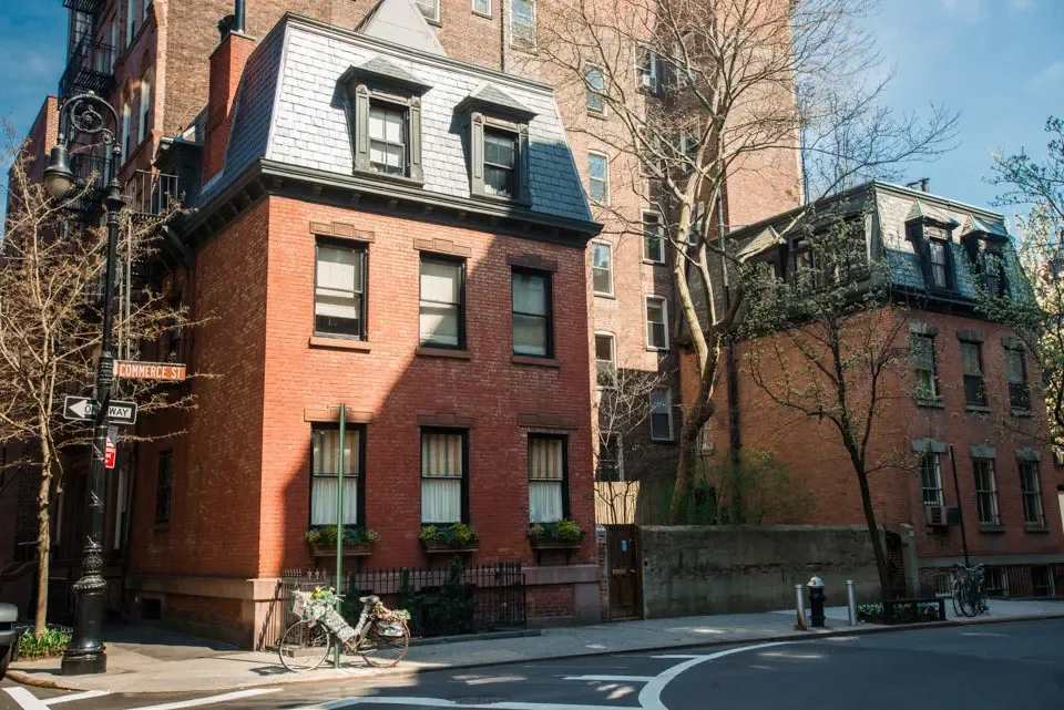 West Village red-brick townhouses with slate mansard roofs on a sunny street corner.
