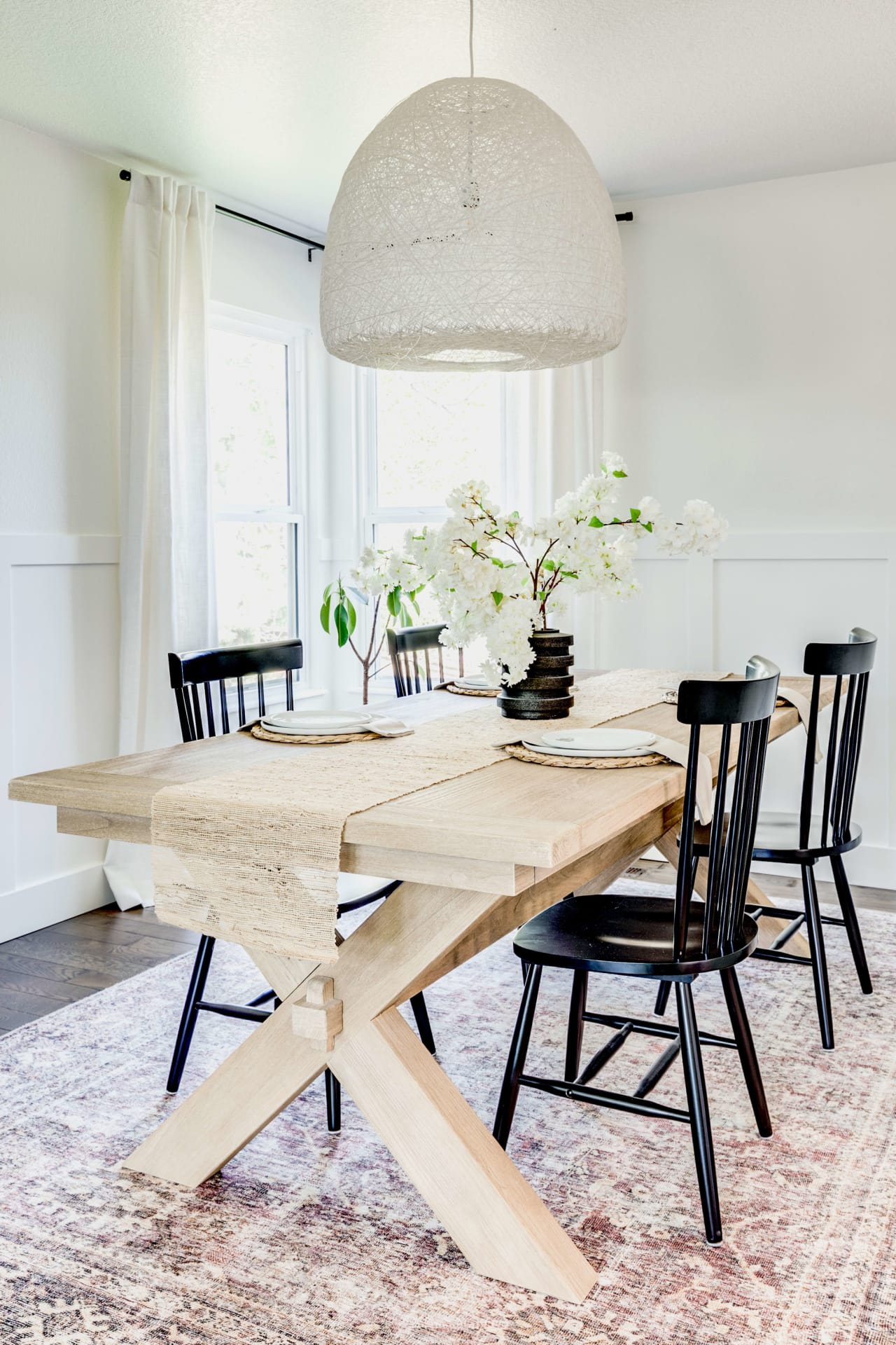 A dining room with a wooden table and black chairs, lit by a white pendant light