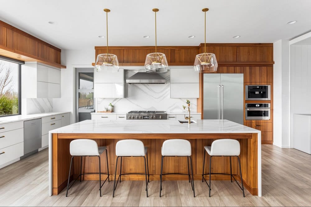 Modern kitchen featuring a large island with marble top, wooden accents, pendant lights, and stainless steel appliances.