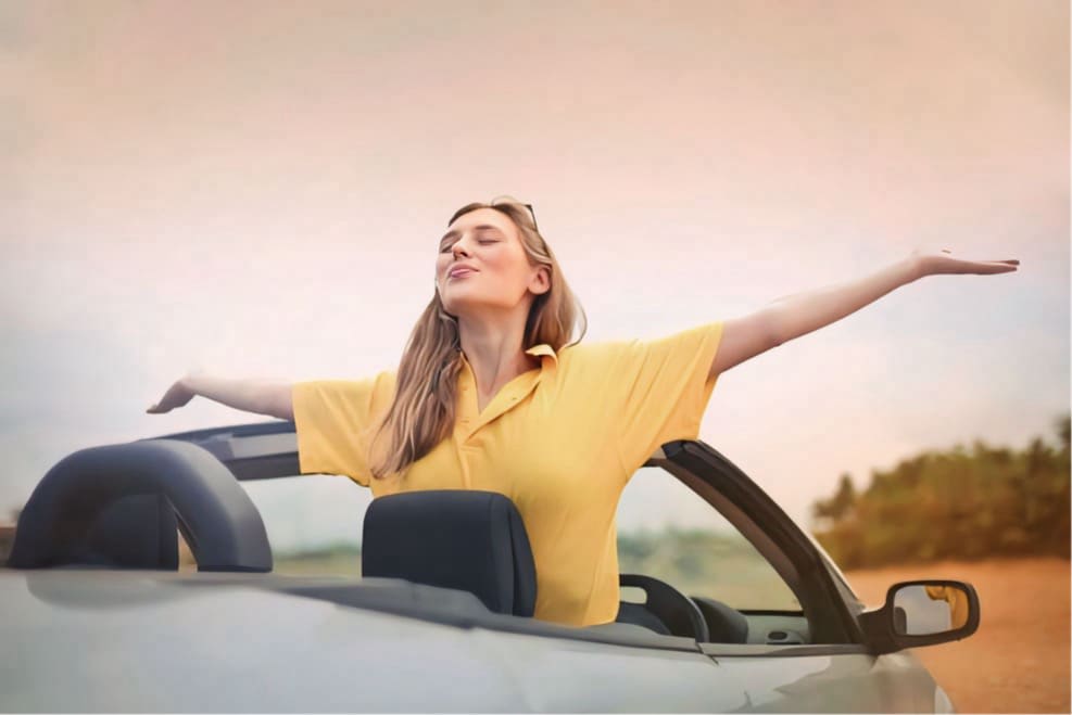 : Woman wearing a yellow t-shirt and holding her arms spread while in a convertible car