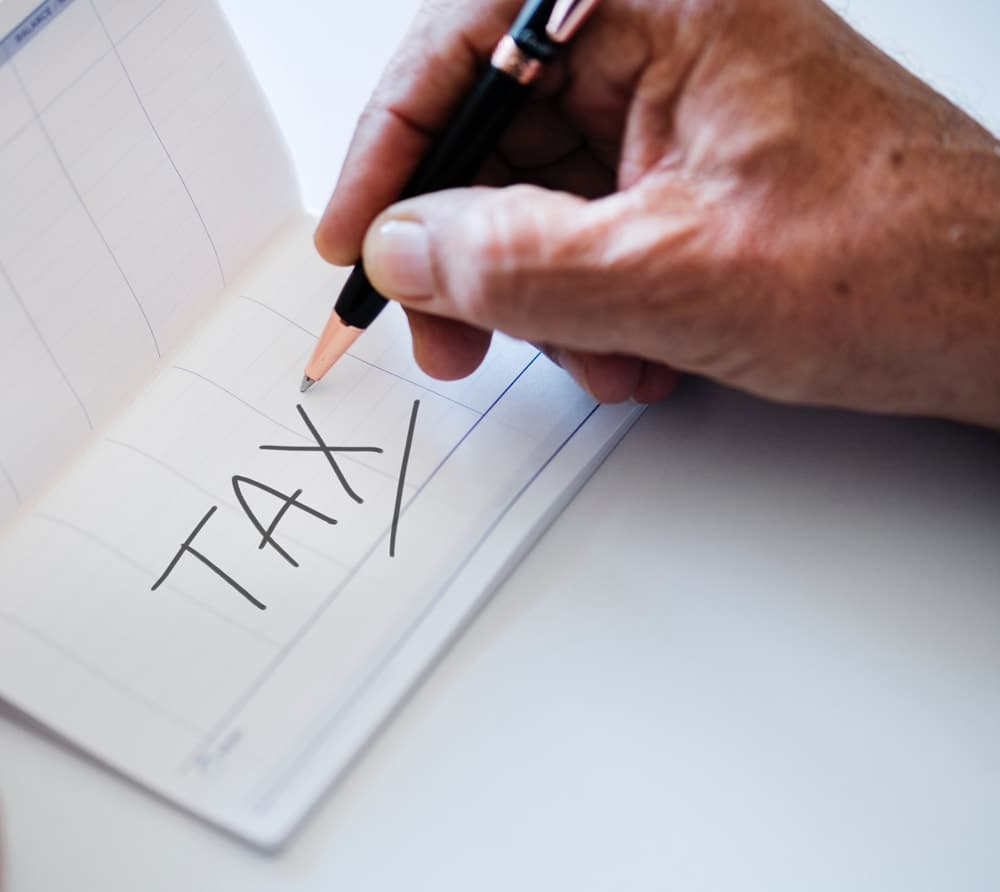 A hand writes “TAX” on a lined planner page.