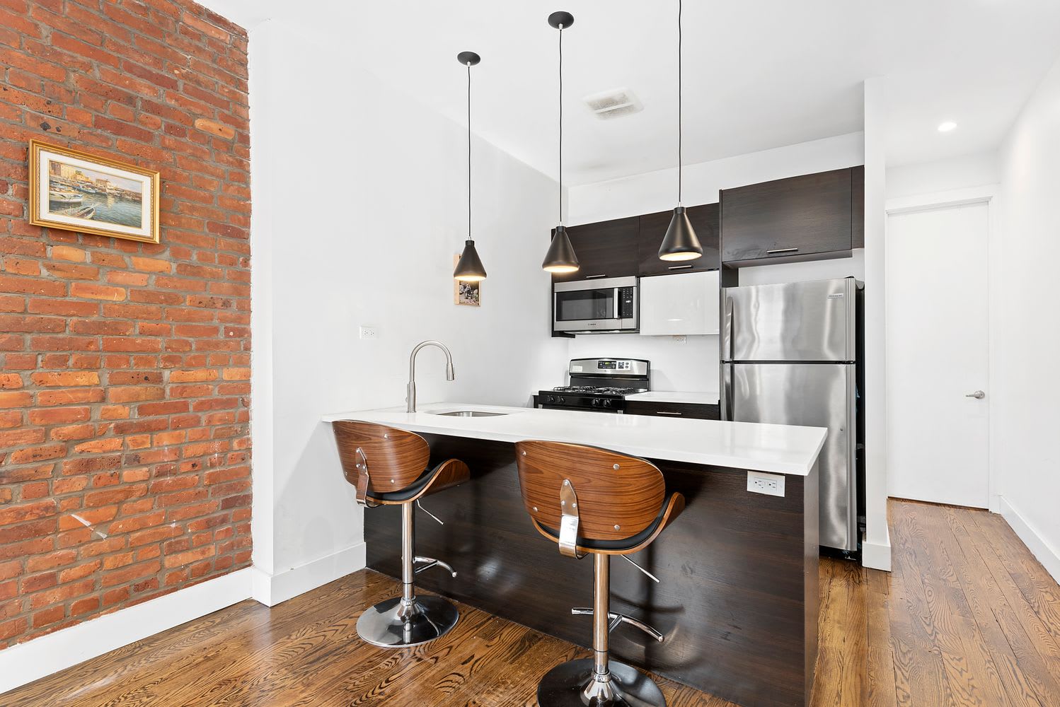 Condo kitchen with an island, stainless steel appliances, and an exposed brick wall.