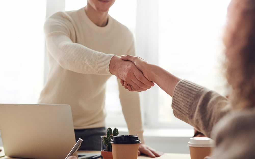 Photo of Two Persons Shaking Hands Over a Laptop on the Table