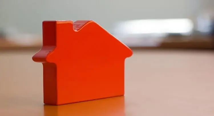 a small red house model on a table, symbolizing real estate, home buying, or investment.