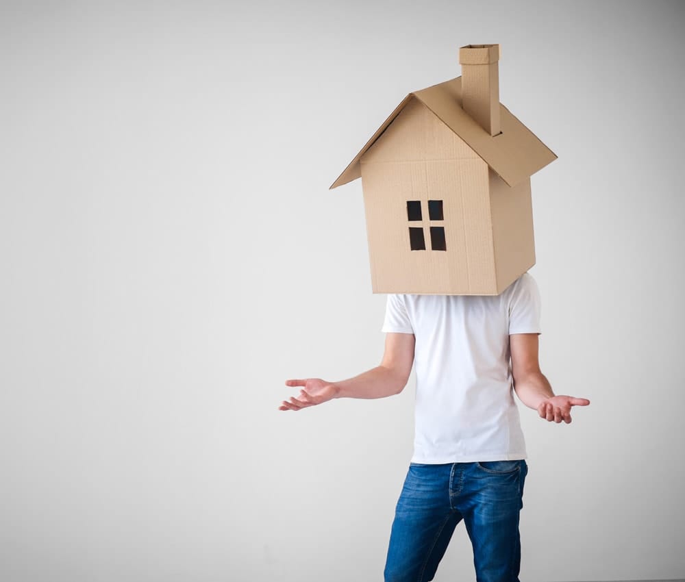 Person wearing a cardboard house over their head, holding both hands out.