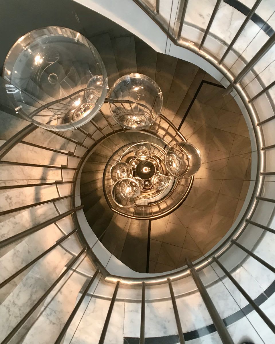 A view looking down a spiral staircase with a chandelier hanging from the ceiling in the center.