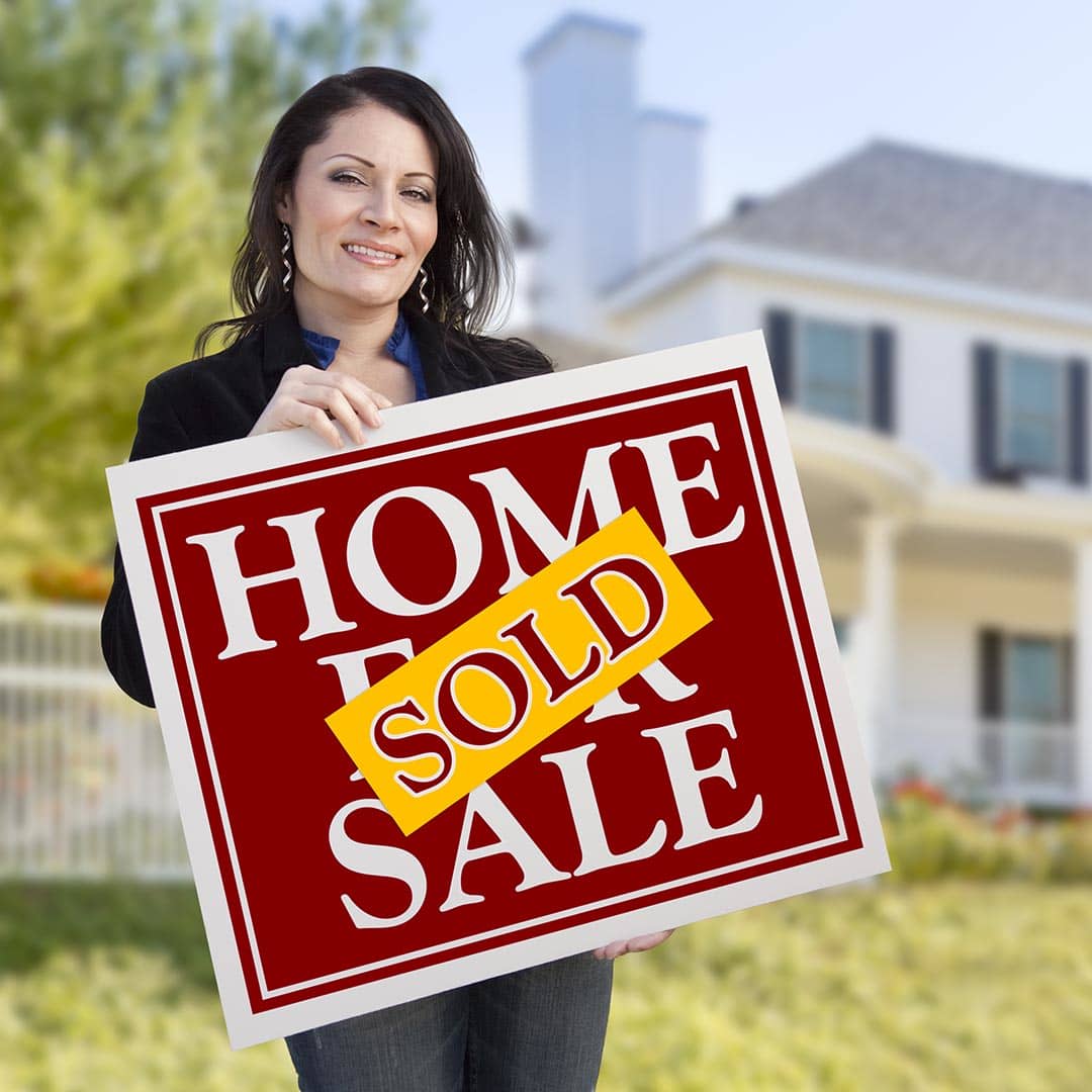 Real Estate agent holding a Sold sign in front of a house
