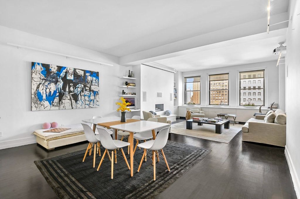 Open-plan living and dining room with contemporary furnishings and city buildings visible through the windows.