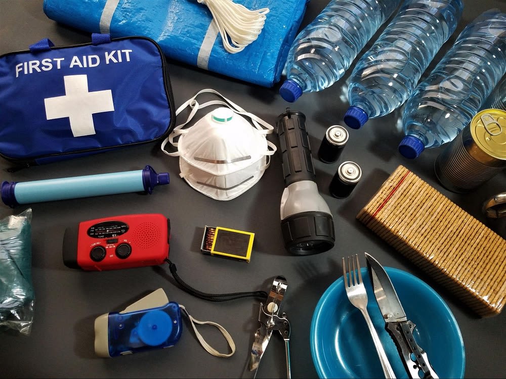 A collection of emergency supplies including a first aid kit, water bottles, flashlight, radio, utensils, and a mask.