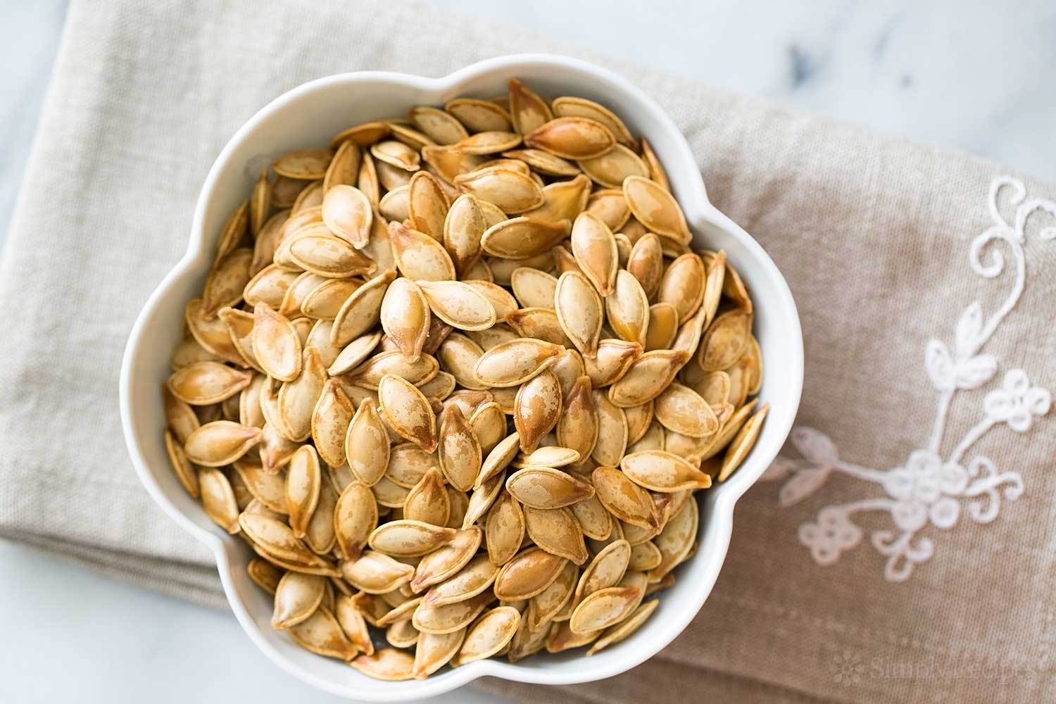 Bowl of pumpkin seeds on beige embroidered linen.