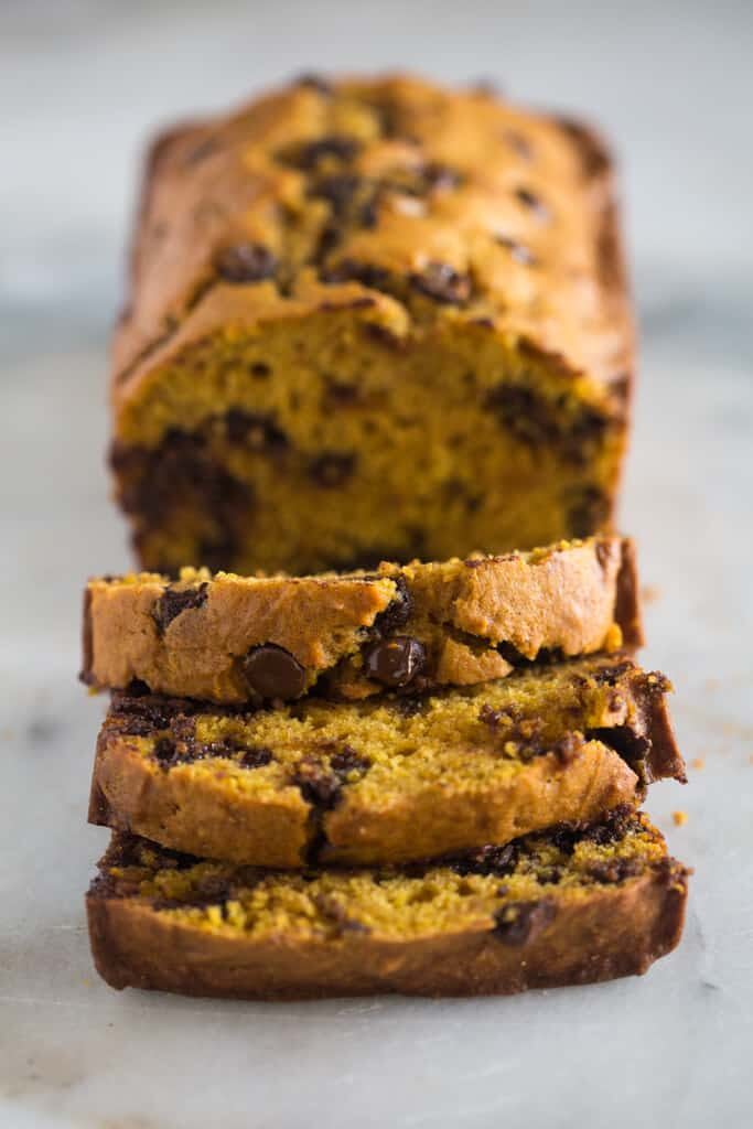 Slices of chocolate chip pumpkin bread stacked in front of the loaf.