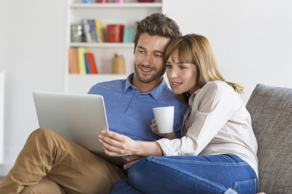 Couple sitting on a couch looking at a laptop together.