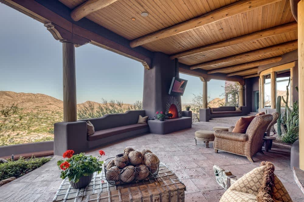 Rustic outdoor living area with wood ceiling, stone fireplace, and panoramic mountain views.