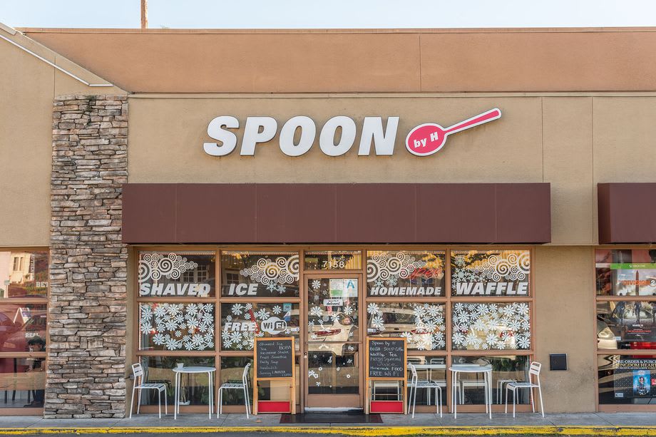Spoon by H storefront with a stone-faced column and windows advertising shaved ice and waffles.
