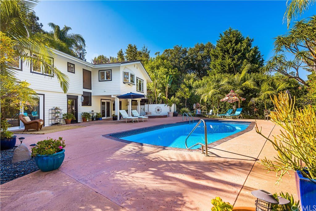 Backyard with lush landscaping, pool, and large home.