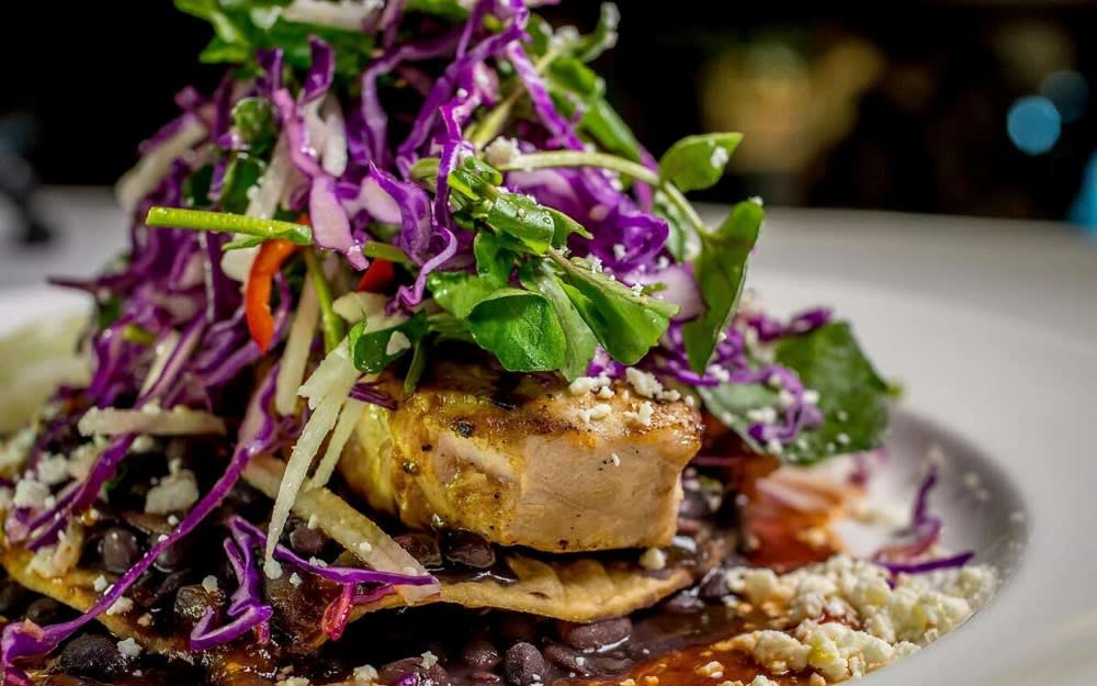 Close-up of a gourmet tuna dish topped with fresh greens and purple cabbage slaw, served with black beans.