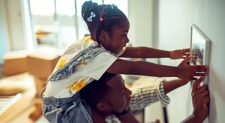 A parent and child working together to hang a picture frame on a wall. The scene is warm and domestic, highlighting family activities and home decoration.