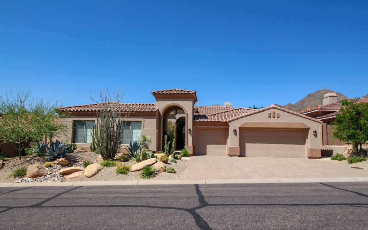  Chill desert home with terracotta roof, arched entry, and rocks.