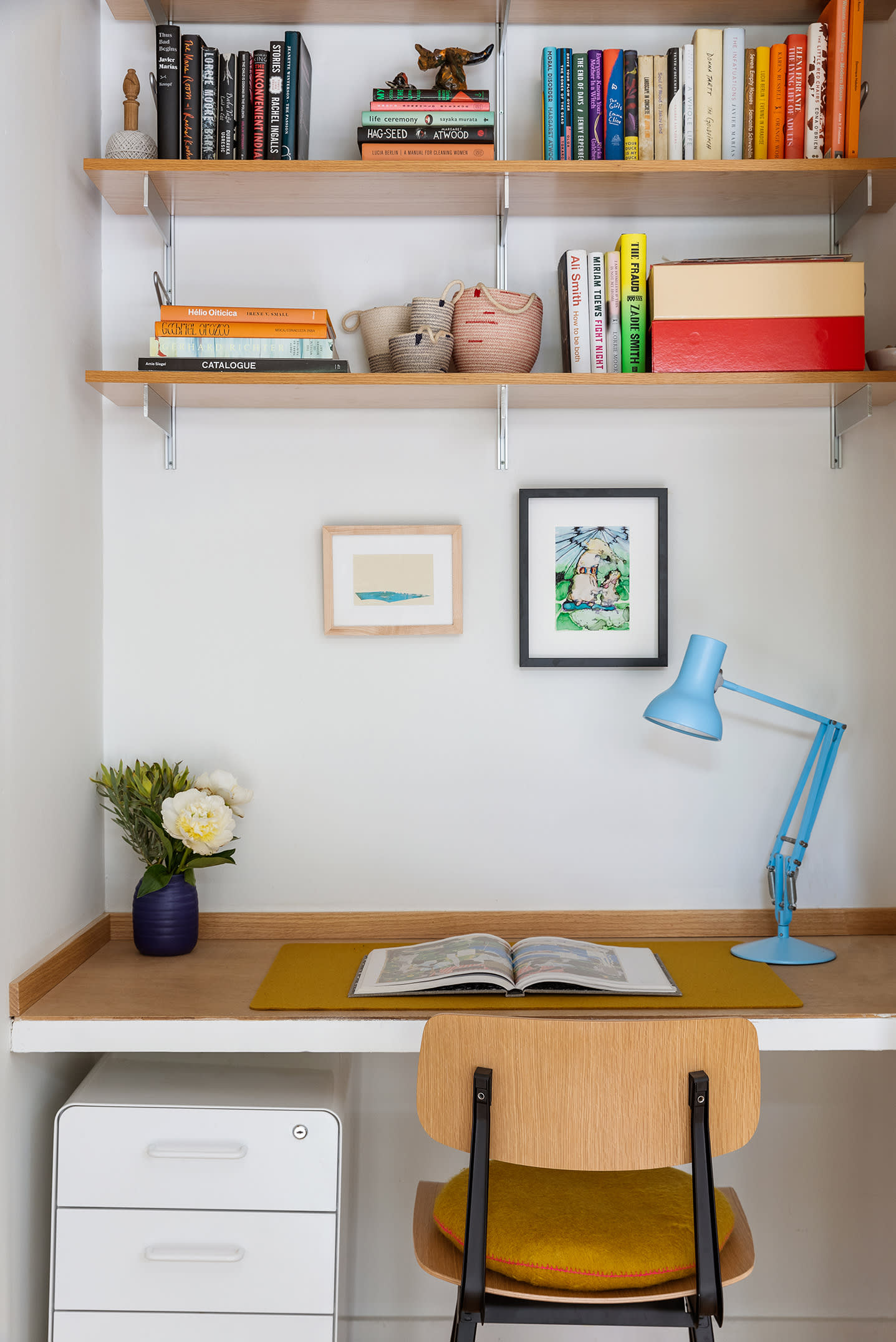 Condo office nook with book-filled shelves, a built-in wood desk, blue lamp, and wooden chair.