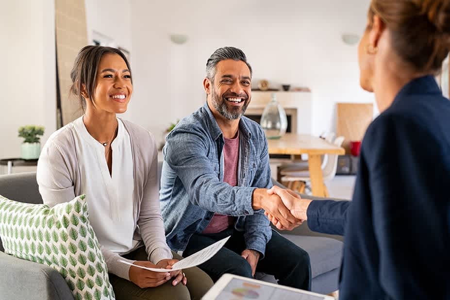 Mature indian man shaking hands with financial advisor at home. Happy smiling couple greeting broker with handshake at home. Multiethnic mid adult man and hispanic woman sealing a contract