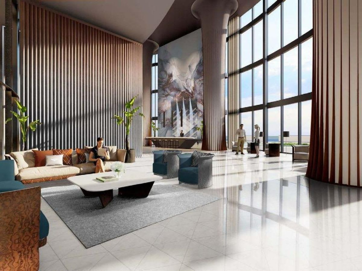 Double-height residential lobby with sculptural seating, a dramatic stone wall, and floor-to-ceiling windows overlooking the water.