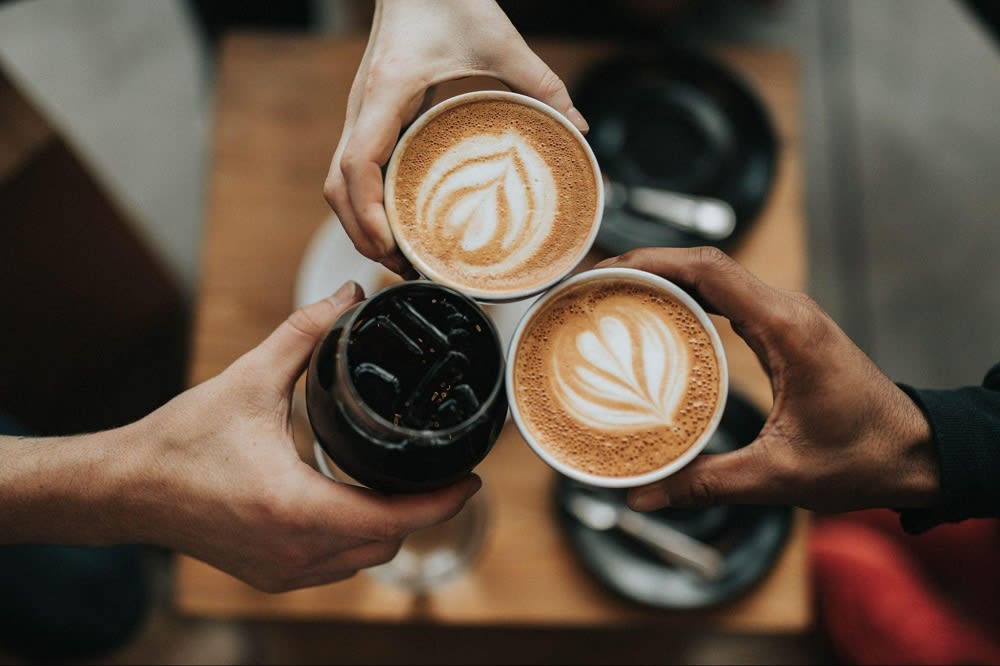 3 mugs of coffee, touching in a toast. 2 have latte art, and the other is iced