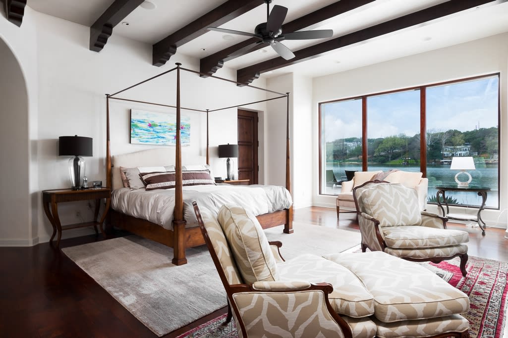 A cozy bedroom with a canopy bed, chairs, and a ceiling fan.