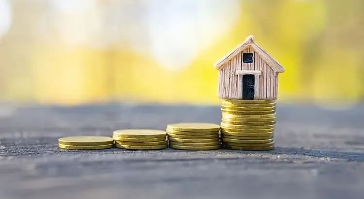 A small house model placed on top of stacks of coins, symbolizing financial savings for a home or investment in real estate.