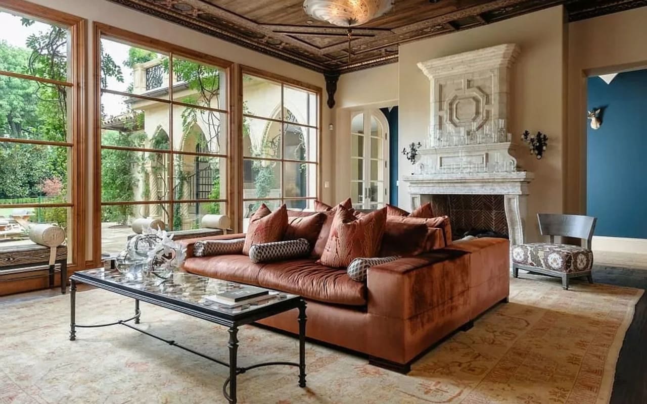 Welcoming living room with a hand-carved fireplace, plush orange sofa, and a picturesque view of the lush backyard.