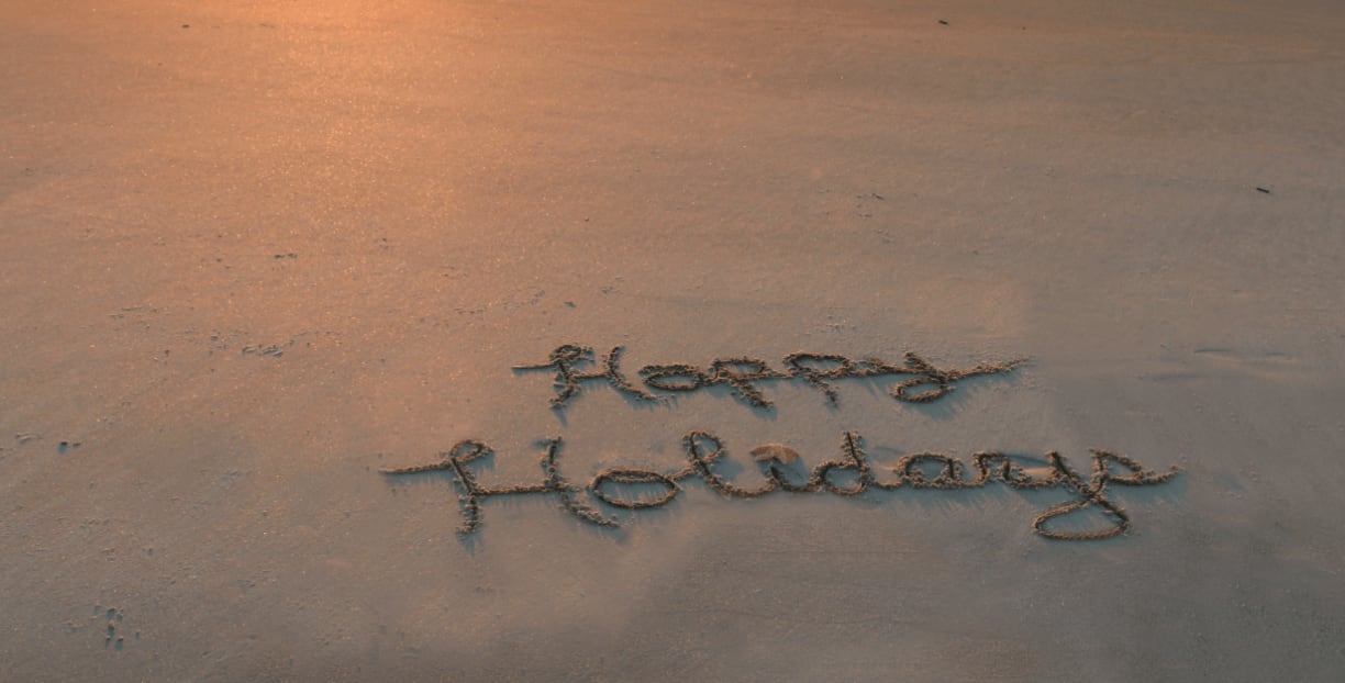 Words 'happy holidays' handwritten in the sand on a Los Cabos beach at sunset