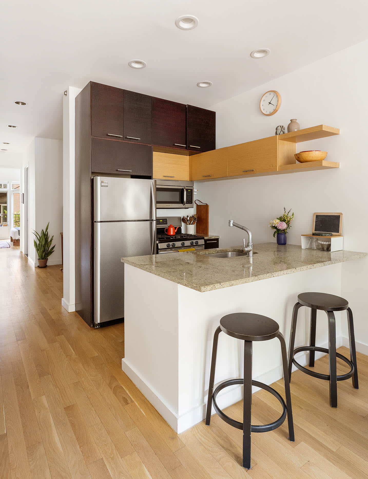 Modern apartment kitchen with a stone island, two bar stools, and dark and light wood cabinets.